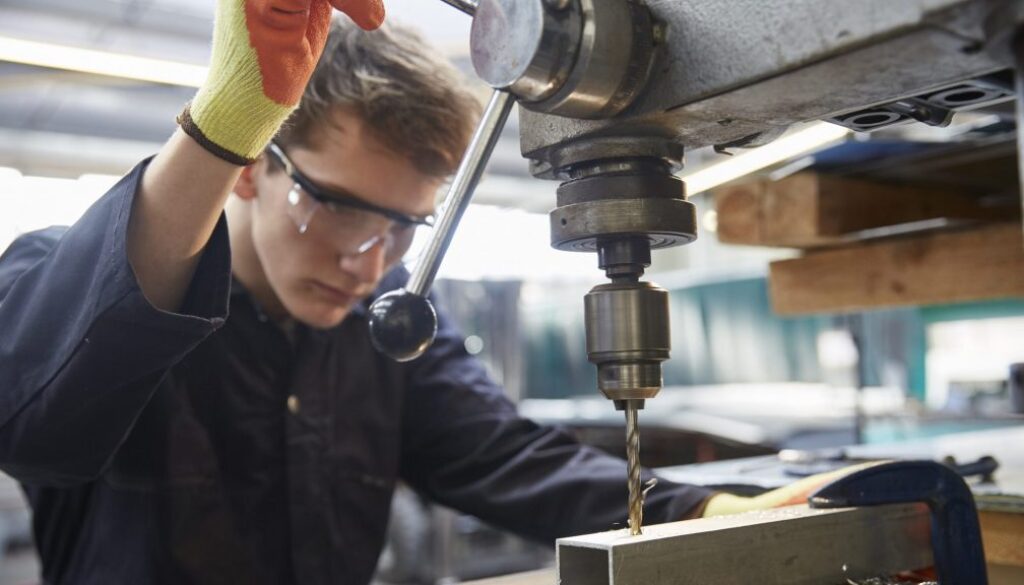 Young apprentice using pillar drill in steel fabrication factory