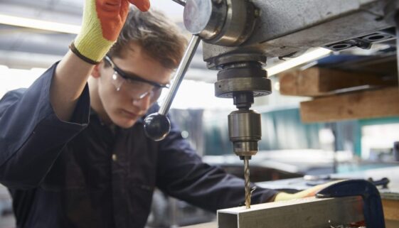 Young apprentice using pillar drill in steel fabrication factory