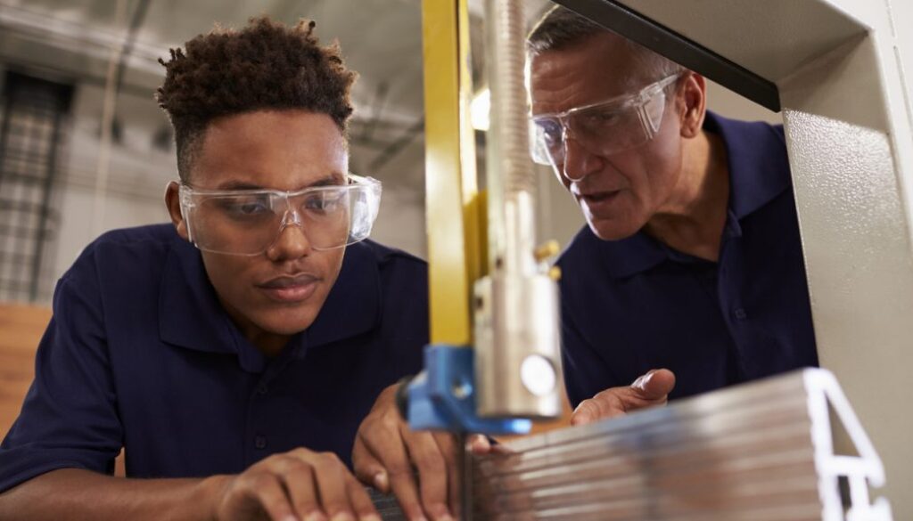 multicultural Carpenter Training Male Apprentice To Use Mechanized Saw