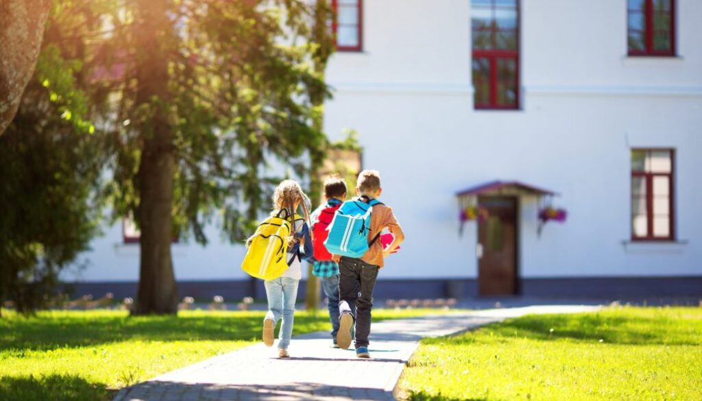 Children with rucksacks running in the park near school